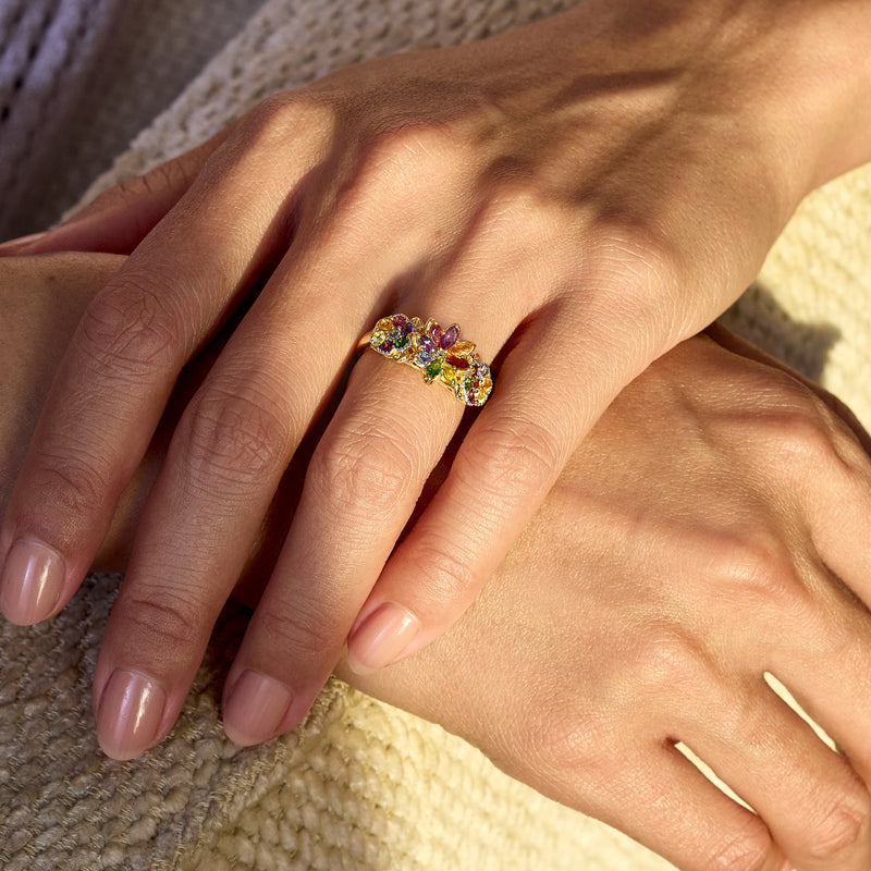 Hand showing gold floral multi-gem ring with small purple and green stones