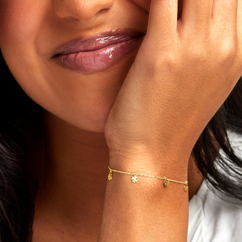 Yellow gold clover charm bracelet on wrist with small clovers along the chain