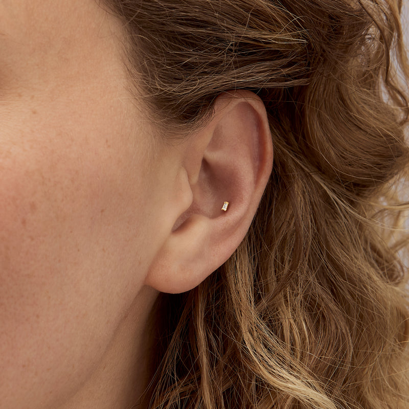 Yellow gold baguette diamond stud earring close-up on ear
