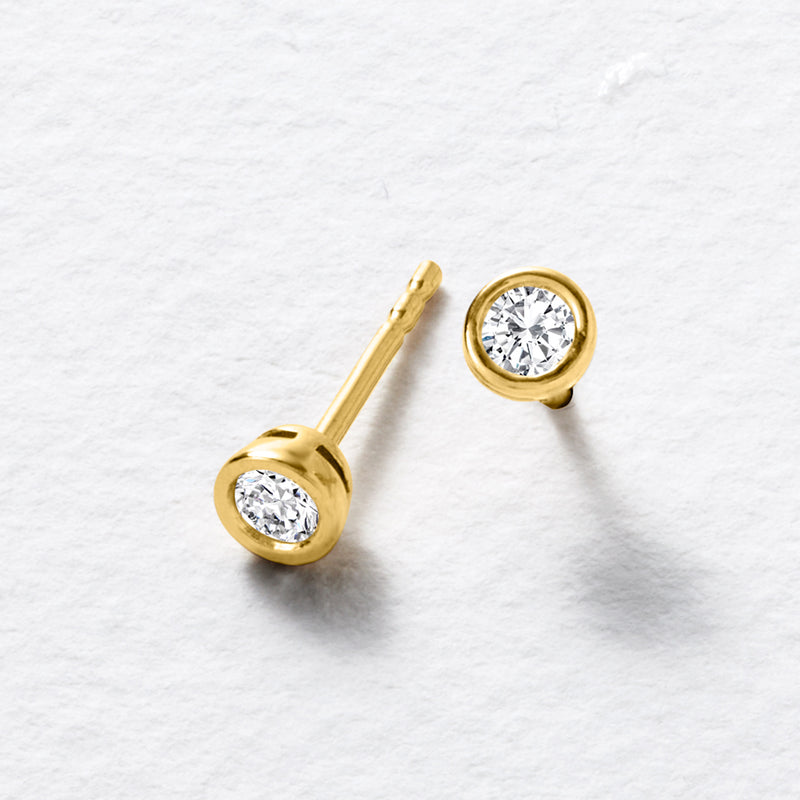 Pair of lab-grown diamond stud earrings with round stones in gold bezels and posts.