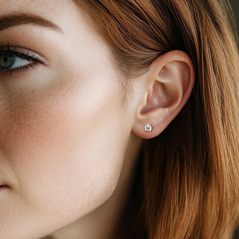 Round diamond stud earring with gold-tone bezel, worn on ear