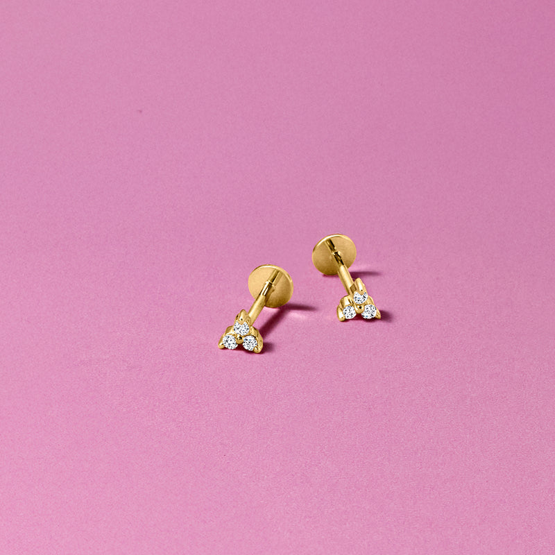 Three-stone diamond stud earrings on ear with 14kt yellow gold flat-back posts