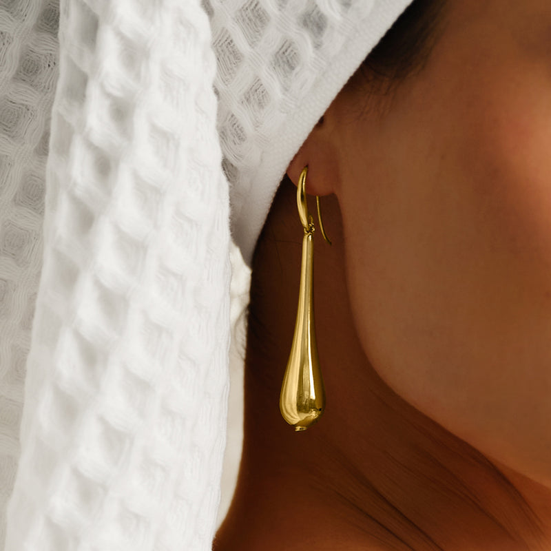 Elongated teardrop yellow gold drop earring with hoop earwire on model.