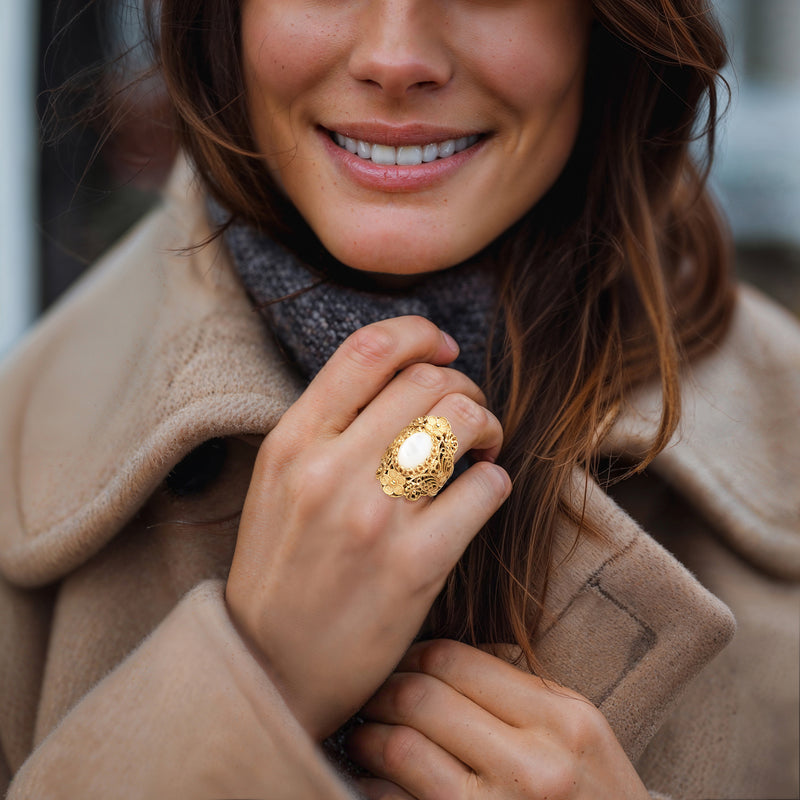 Mother-of-pearl oval gold filigree ring on hand against a beige coat cuff