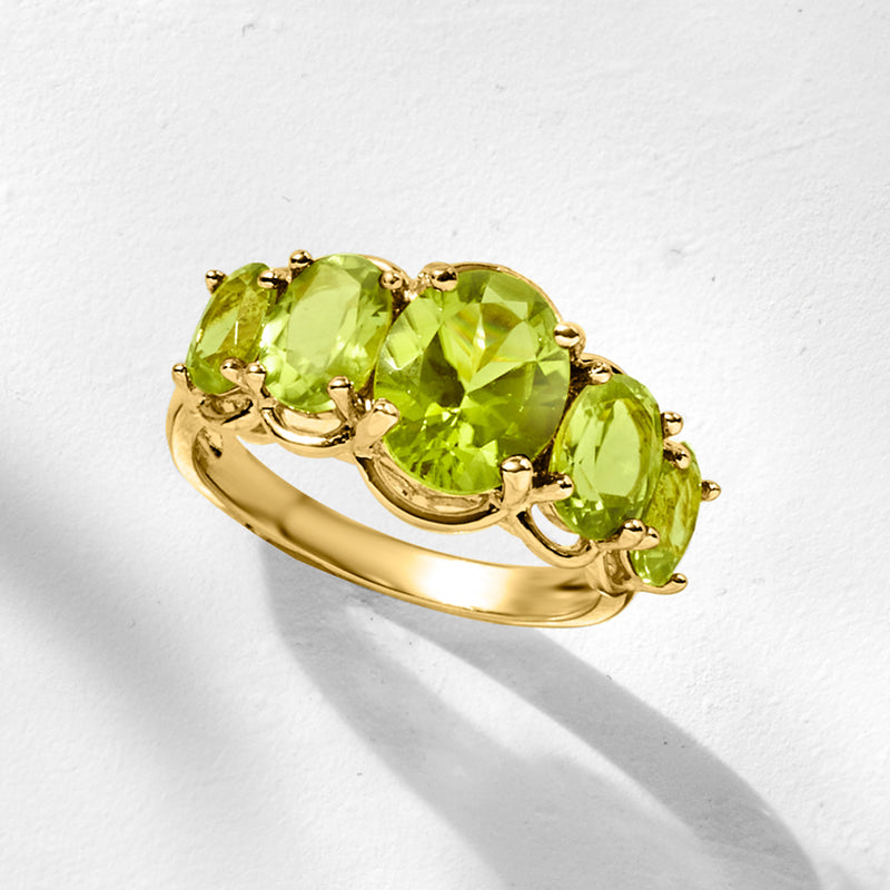 Peridot five-stone ring with five oval green gemstones in a gold bezel setting