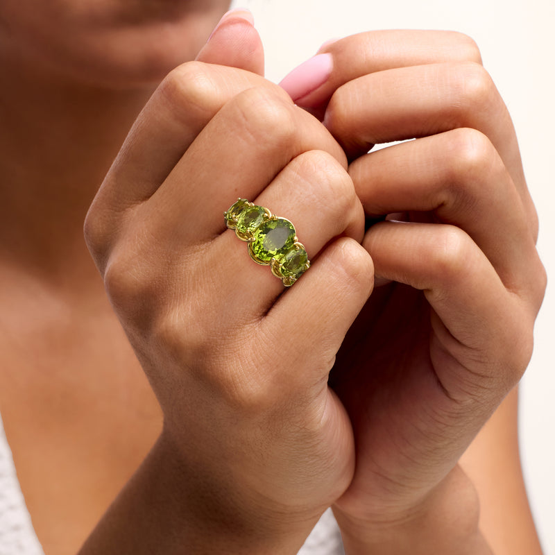 Peridot five-stone ring on finger with three oval green gemstones