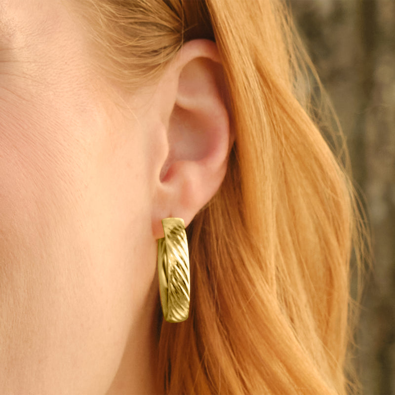 Textured yellow gold hoop earrings shown on a pierced ear