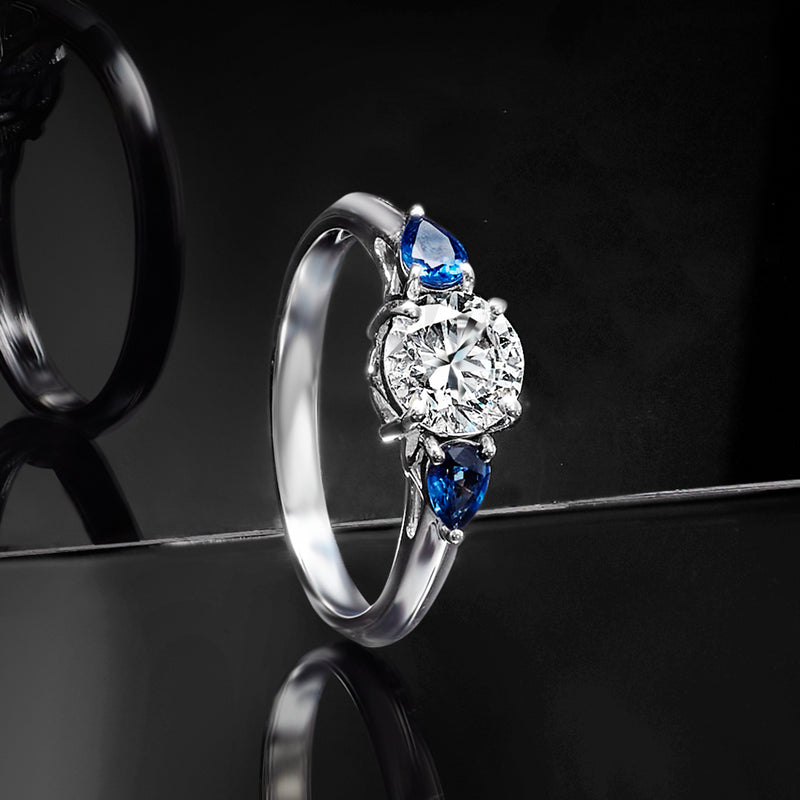 14kt white gold ring with round diamond center flanked by pear blue sapphire stones