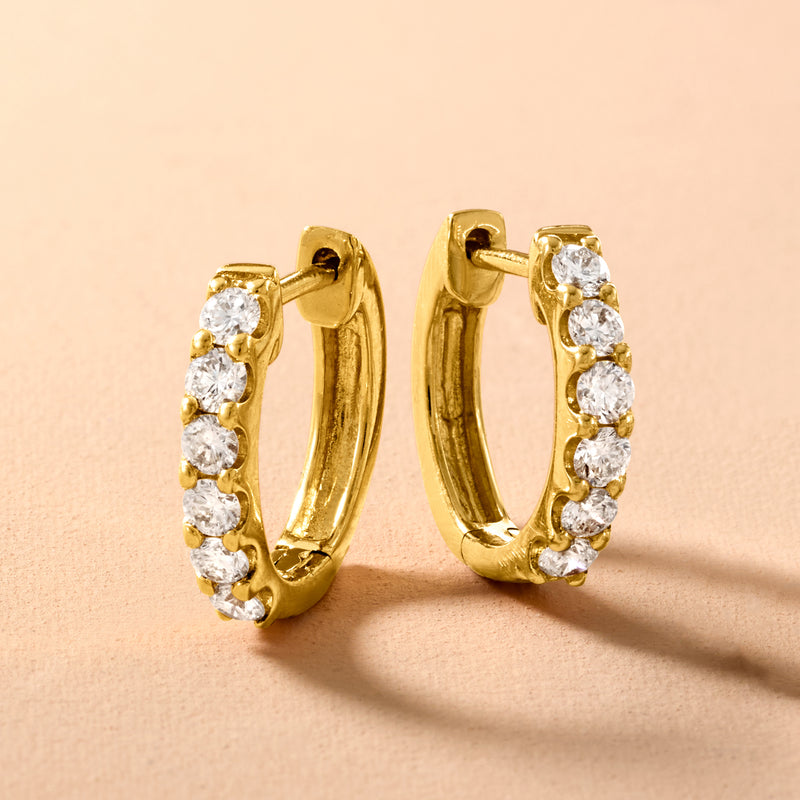 Gold huggie hoop earrings with white round diamonds set in a row, close-up
