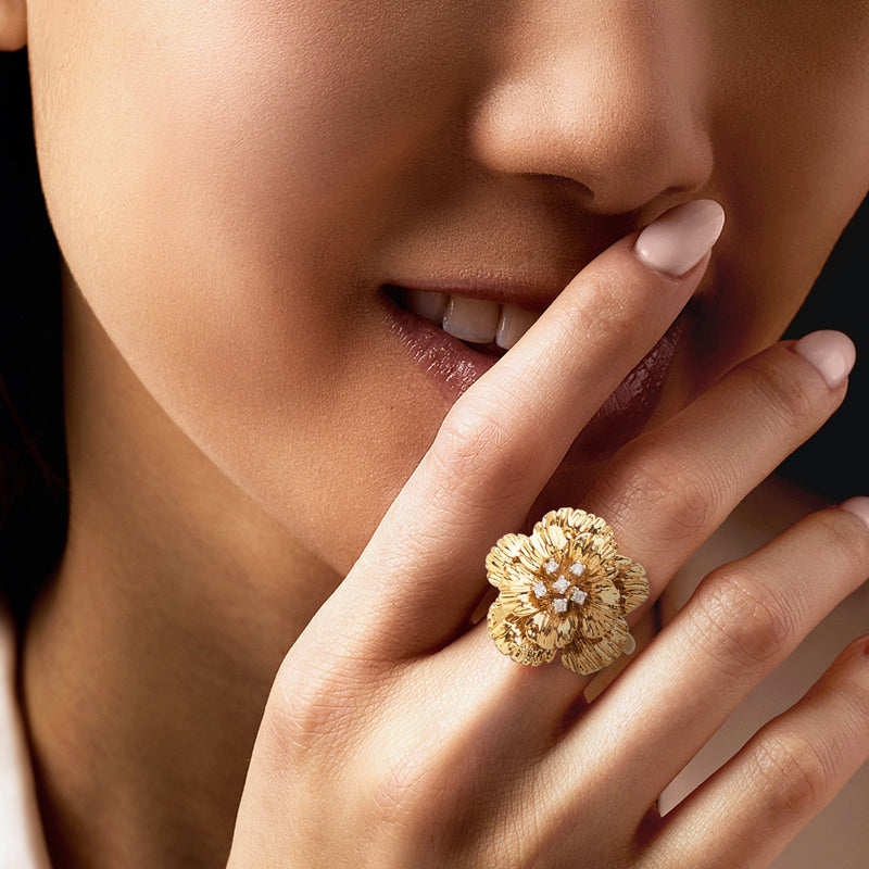 Gold flower ring with sparkling stones on finger, shown in close-up
