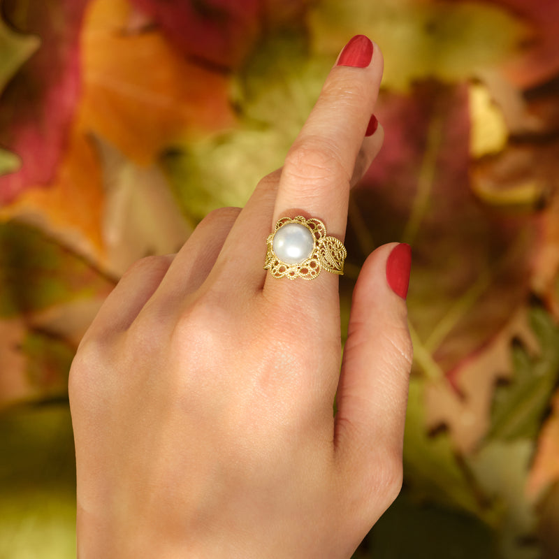 Gold filigree cultured pearl ring worn on finger, round white pearl in center