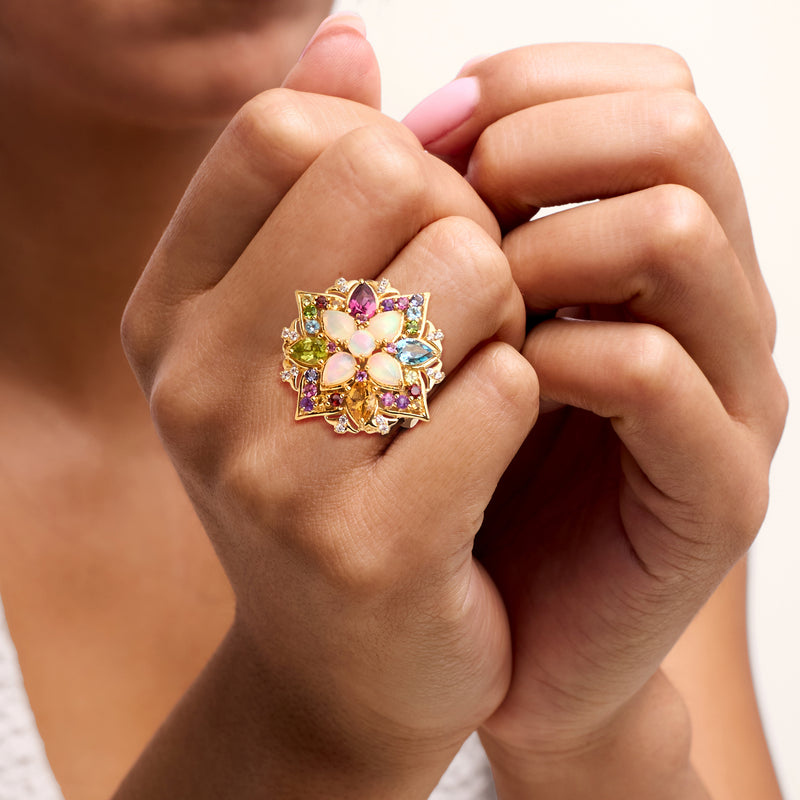 Multi-gemstone ring on finger, gold tone with opal-like center and pink, green, blue accents