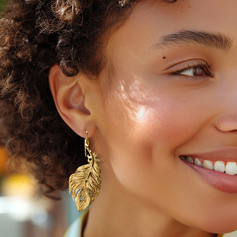 Worn gold feather drop earrings with ornate filigree leaf details
