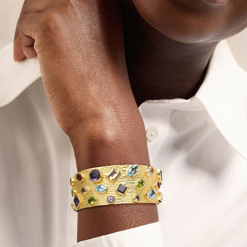 Gold gemstone cuff bracelet worn on wrist, multicolor stones set in gold.