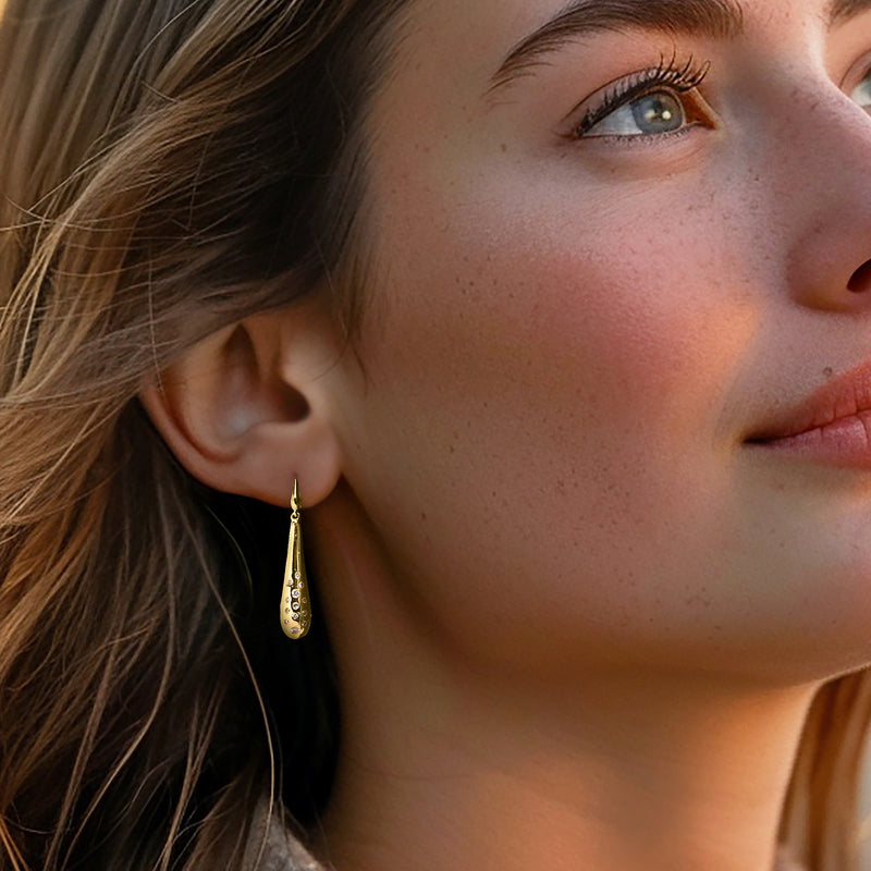 Yellow gold teardrop drop earrings with round diamond cluster, worn