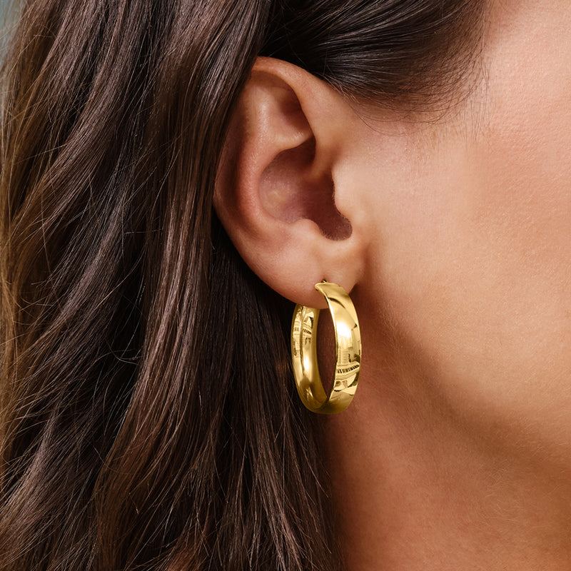 Yellow gold hoop earrings worn on ear, thick polished round hoops