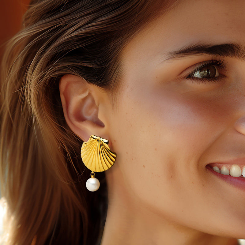 Gold scallop-shell hoop-style drop earrings with a white pearl, on-ear profile.