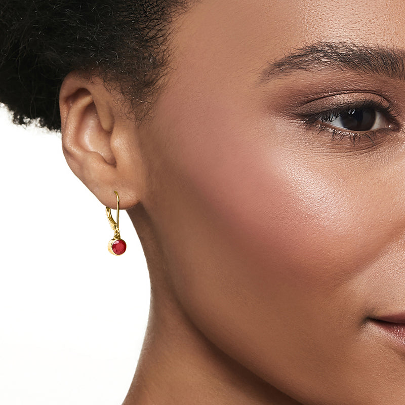 Gold leverback ruby drop earrings on ear, round red stones.