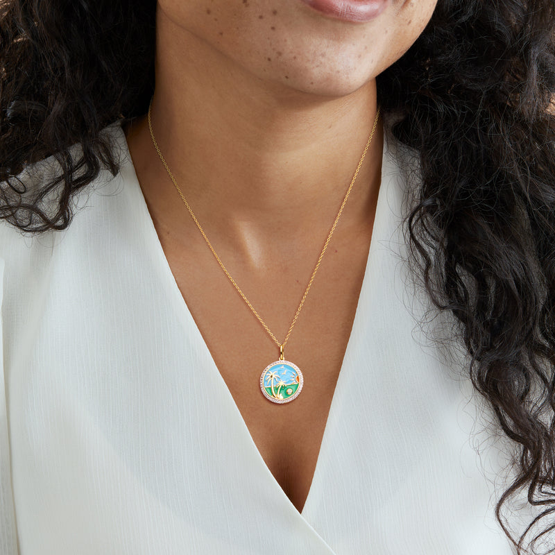 Gold-tone pendant necklace worn with small round blue enamel scene and palm trees
