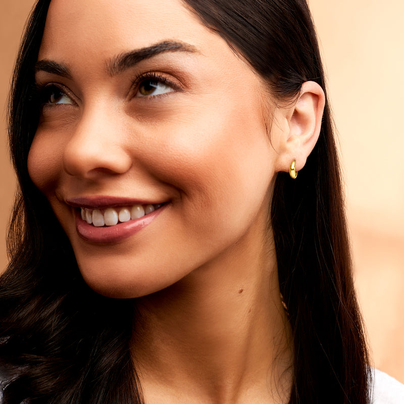 Huggie hoop earrings in yellow gold on ear, small round hinged hoops