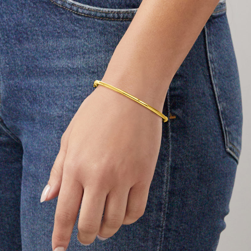 Slim polished 10kt yellow gold bangle bracelet on wrist, smooth oval hoop
