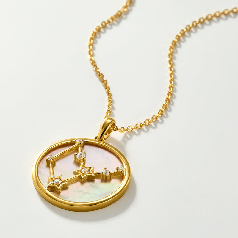 Gold zodiac pendant necklace close-up with round mother-of-pearl and white topaz stars