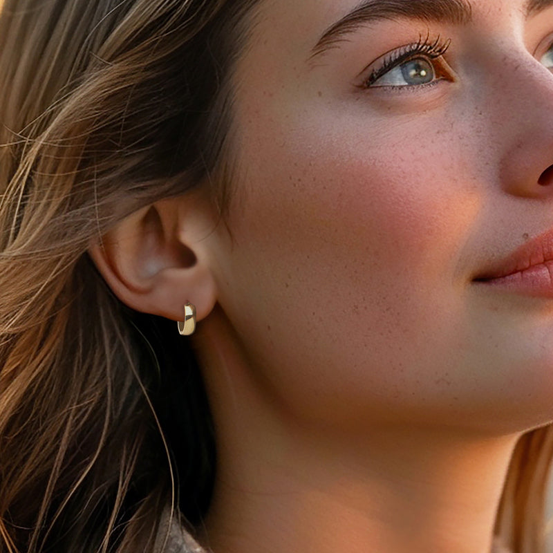 Petite yellow gold huggie hoop earrings on a wearer, one earring visible