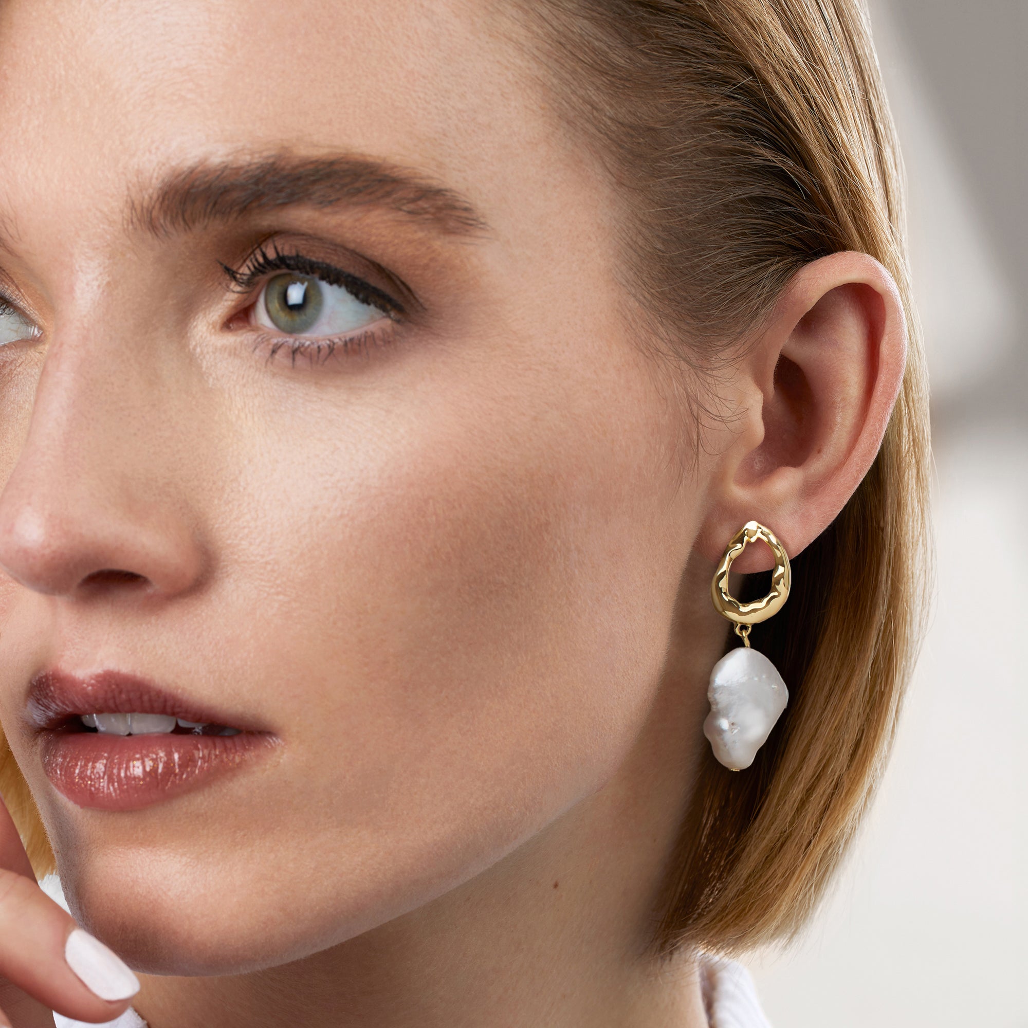 Gold drop earrings with baroque cultured pearl drops on model's ear, scalloped hoops