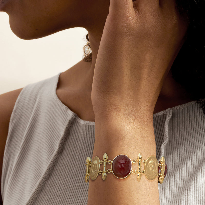 Gold-tone bracelet on wrist with red oval scarab cabochons and hinged link design