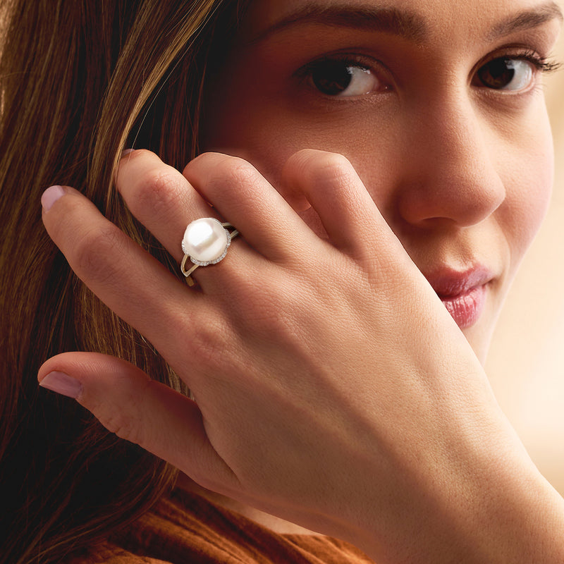 Gold ring with white cultured pearl and diamond halo, worn on finger