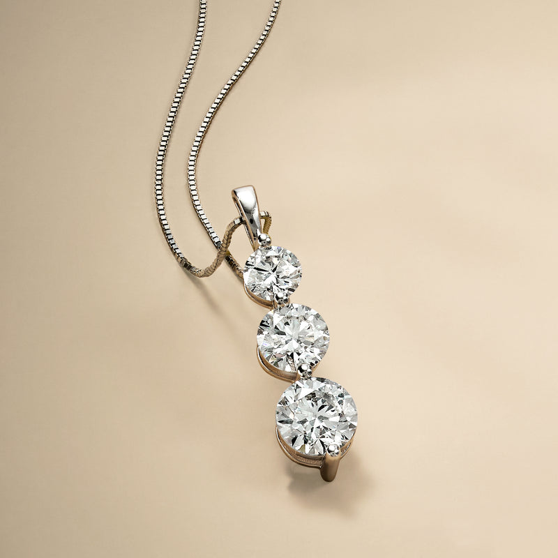 Three-stone diamond pendant necklace with prong-set round stones, angled view