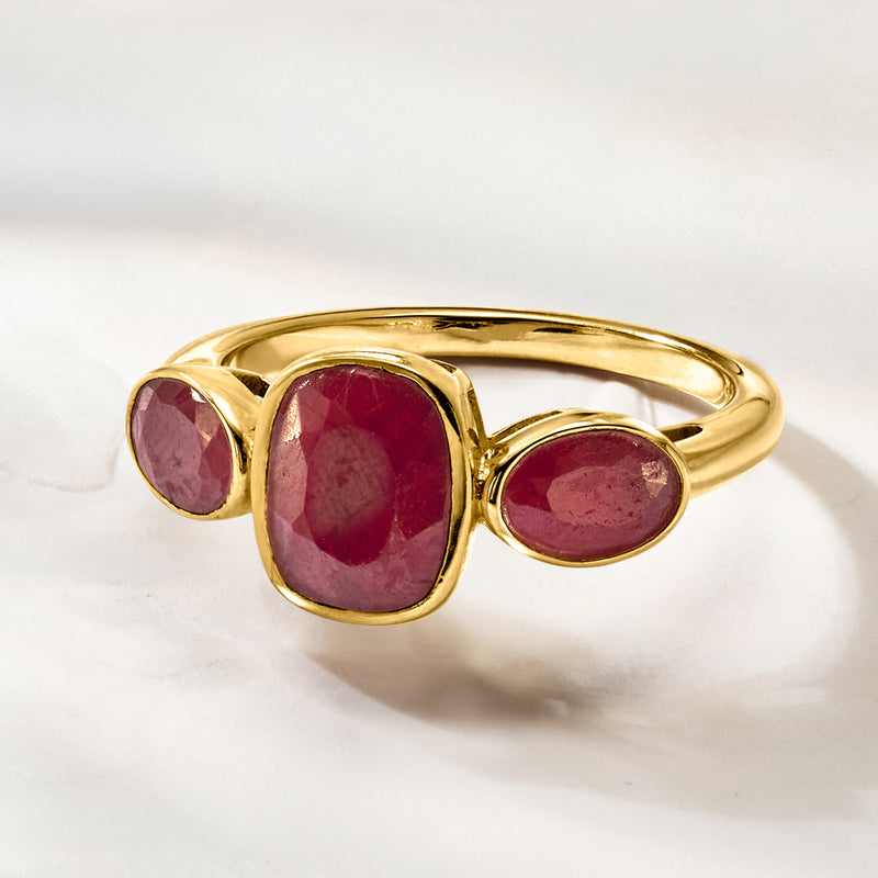 Three-stone ruby ring angled view with center oval ruby and two side rubies in gold