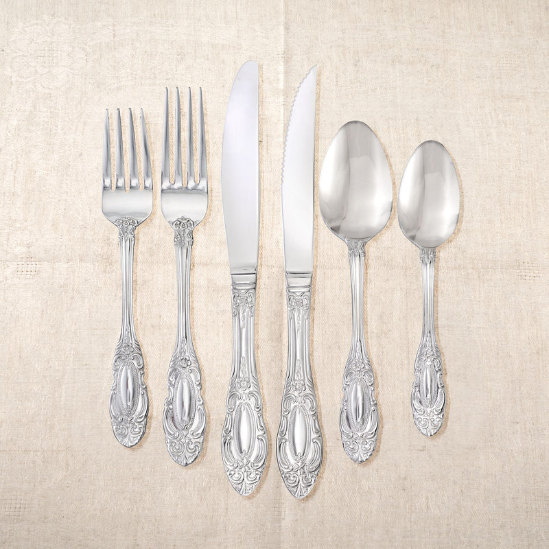 Stainless steel flatware set with ornate scrolling handles and shiny spoons and knives