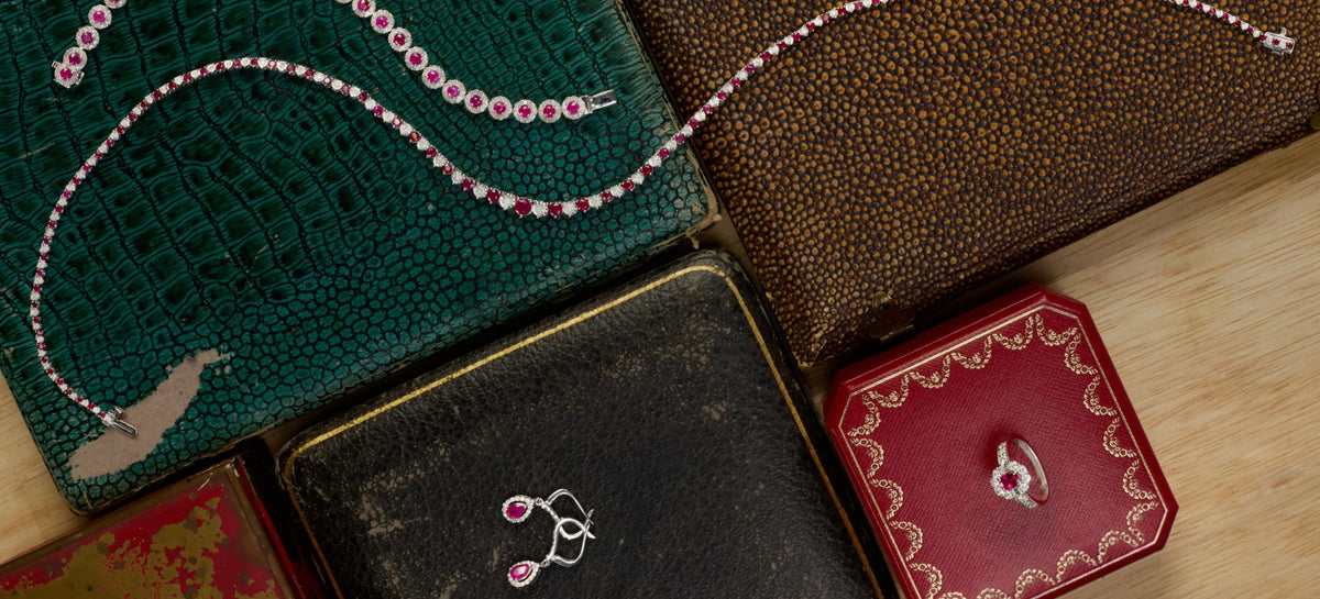 A collection of ruby jewelry sitting on top of dark tones cases on a wooden desk