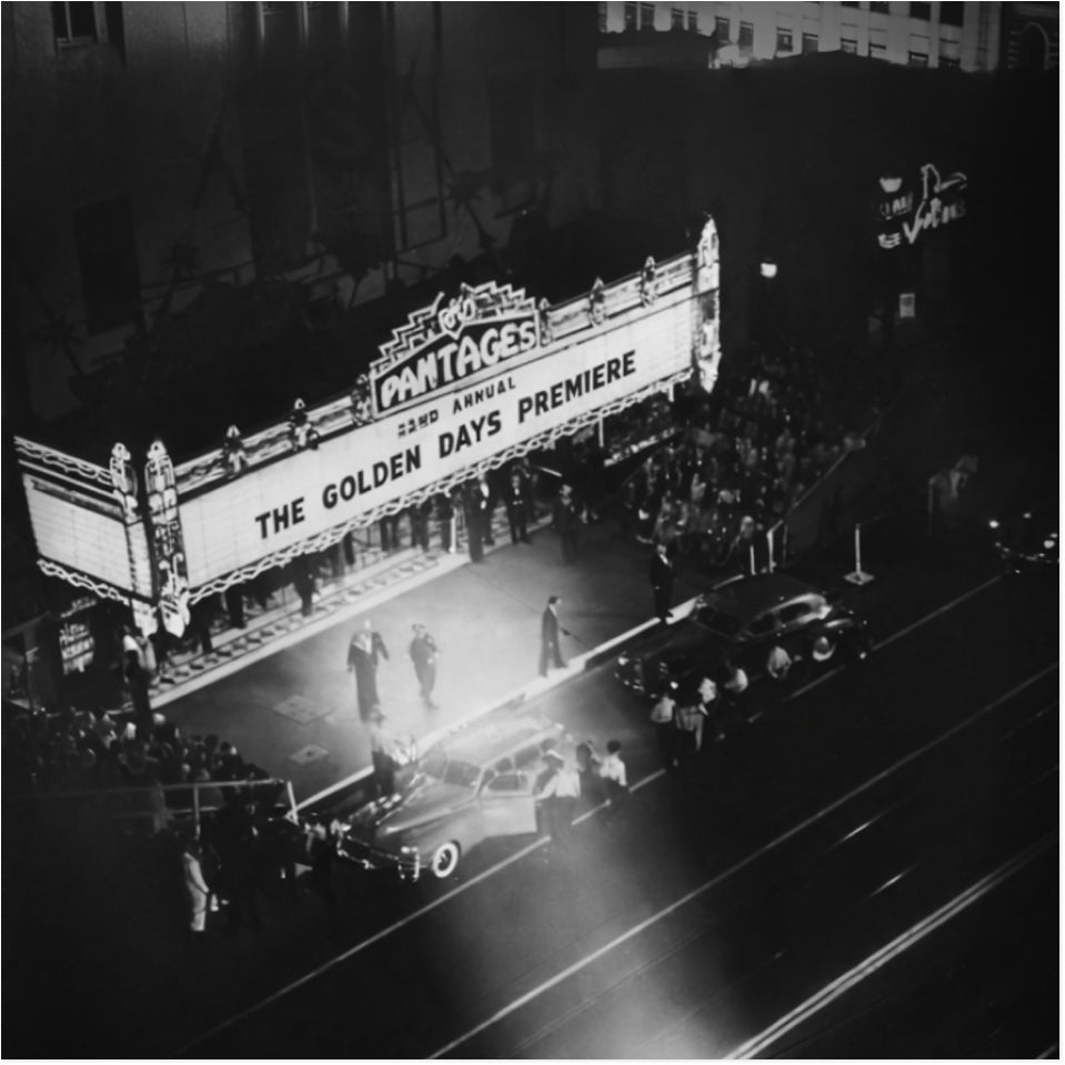 Black and white photo of a movie theatre marquee stating 'the golden days premiere' with people crowding around the entrance and cars dropping people off for a premiere
