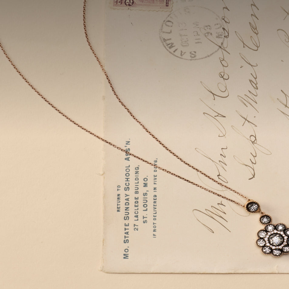 A rose gold chain necklace with a floral cluster pendant featuring clear stones, displayed on a vintage cream-colored letterhead paper.