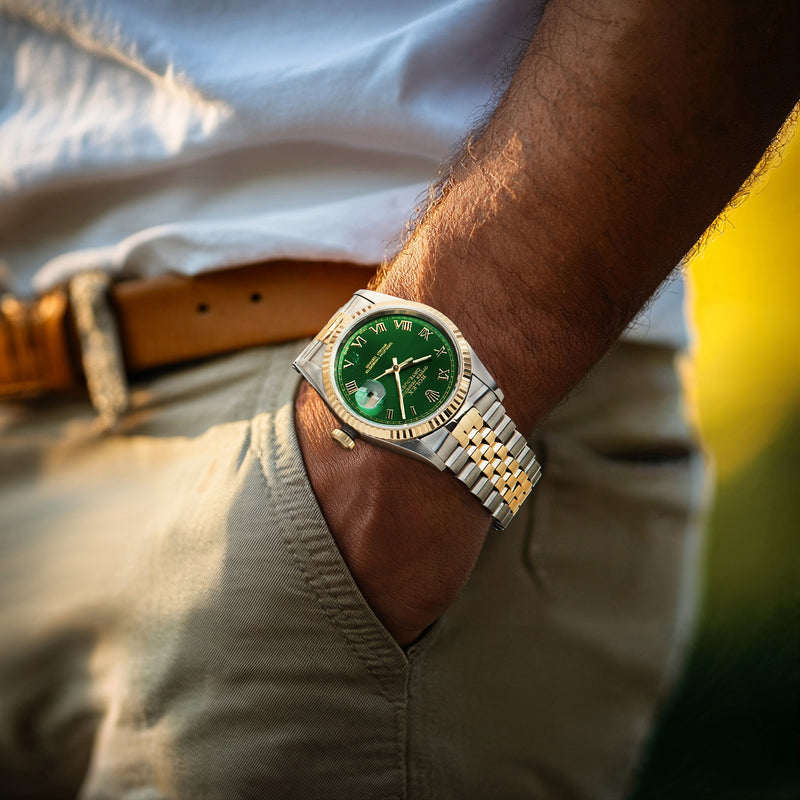 Two-tone stainless and yellow gold watch with green dial on wrist, metal bracelet