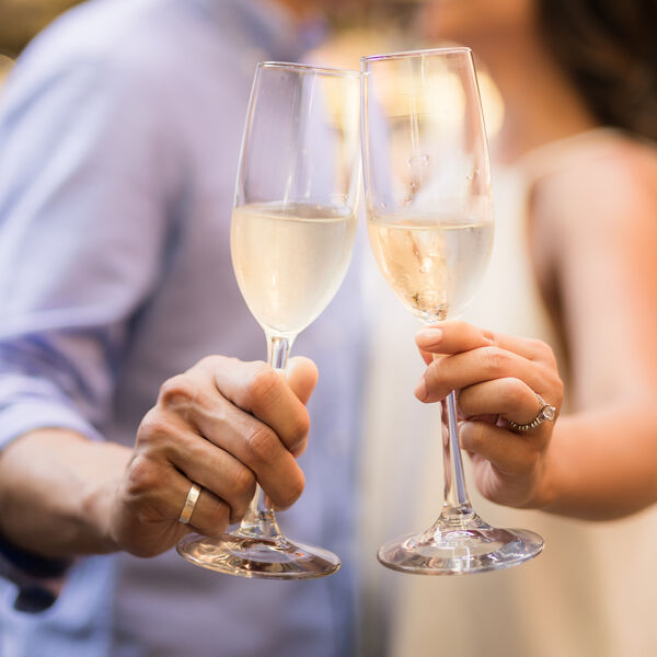 Couple wearing wedding rings holding champagne glasses. Photo by Joshua Chun on Unsplash.com